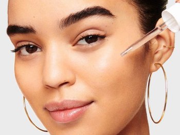 Model applying clear serum to her face.