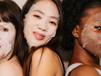 Front shot of a group of 3 diverse women posing while wearing hydrating sheet face masks.