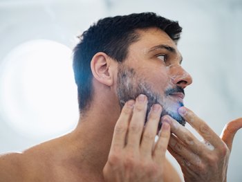 Front shot of man’s side-profile as he washes his sensitive skin with a foaming white, gentle cleanser.