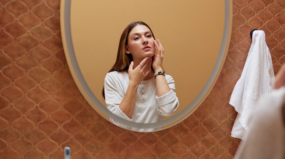 A woman examining her face in a mirror.