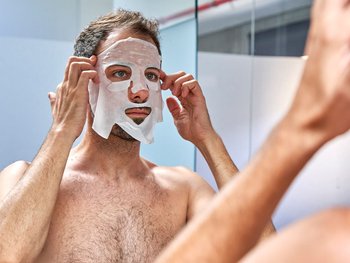A man with a sheet mask on his face, demonstrating how to apply and wear a sheet mask.