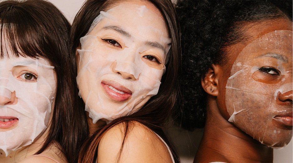 Three diverse individuals smile while wearing sheet masks.