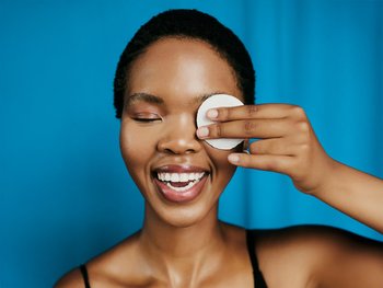 A woman holds a cotton pad soaked in micellar water to her eye, illustrating the gentle makeup removal process.