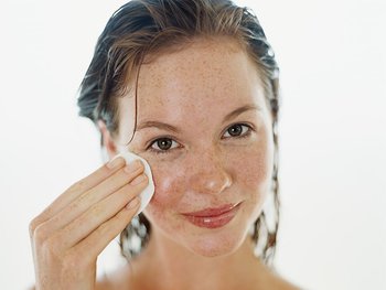 A woman gently wipes their face with a cotton pad soaked in micellar water, illustrating its use as a makeup remover and cleanser.