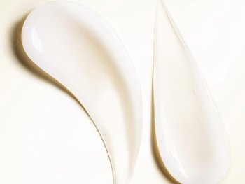 Two swatches of a creamy moisturizer displayed on a smooth, light-colored surface.