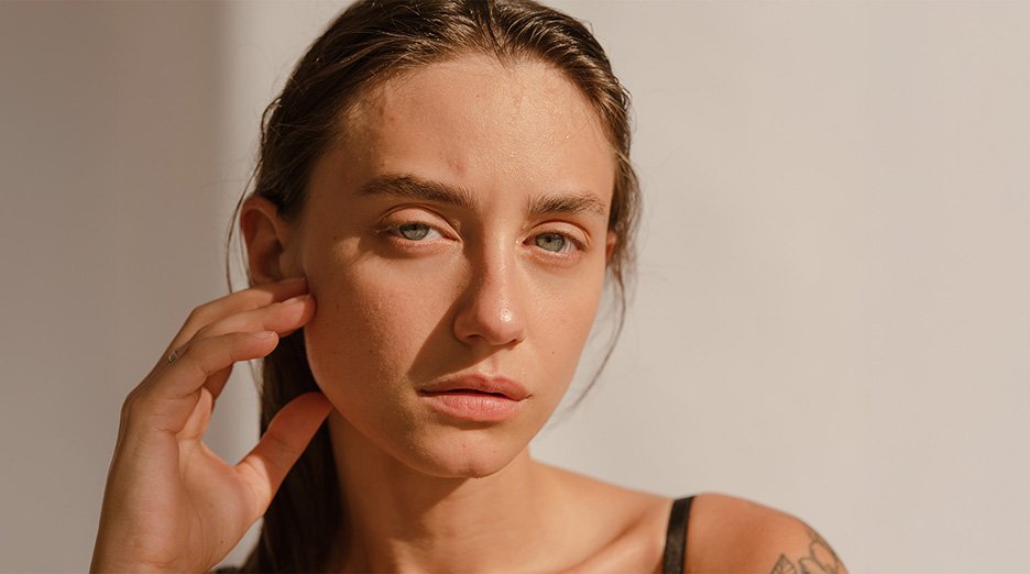 Close up of a woman's face illuminated by the sunlight while her right hand slightly touches her cheek.