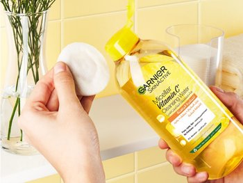 A hand pours Garnier Micellar Water onto a cotton pad.