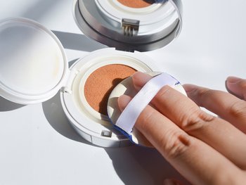 A hand reaches for an open compact of BB cream.