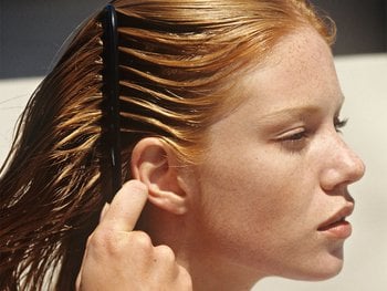 Close of shot of a woman with strawberry blonde hair. She is at about 45 degrees from the camera, combing through her wet hair with a wide-tooth comb.
