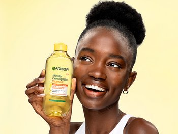 Smiling woman holding a bottle of Garnier Micellar Cleansing Water with Vitamin C formulated for dull, uneven skin to instantly brighten