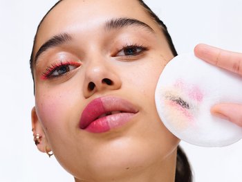 A person uses a cotton round to remove makeup.
