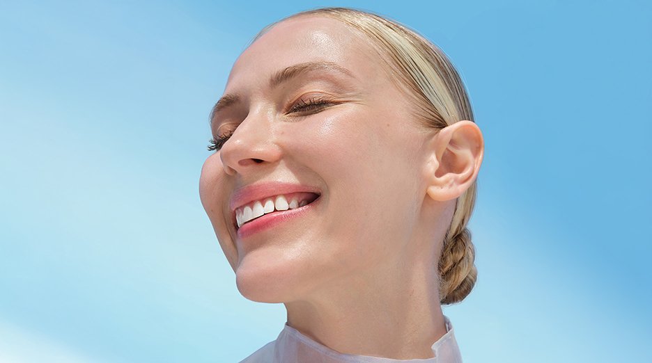 A woman with light skin and pulled-back blonde hair smiles with her eyes closed.