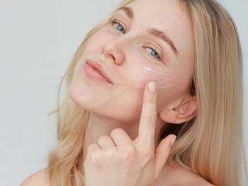 Young woman in her 20s applying serum to her face.