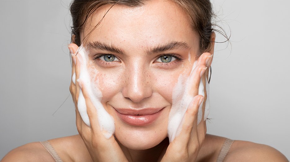 Young girl washing her face while smiling at the camera. She seems to enjoy the amplitude of foam on her face.