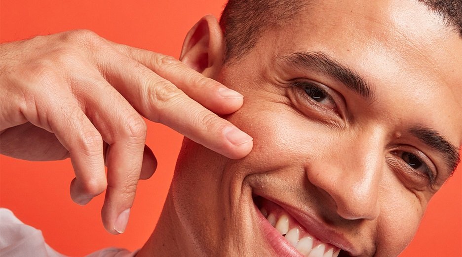 A smiling person touching their face.