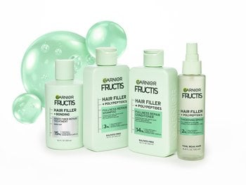 Four Garnier Fructis Hair Filler + Polypeptides products: Fiber Repair Treatment, Fullness Repair Shampoo, Fullness Repair Conditioner, and Thickening Spray, against a background of green bubbles.