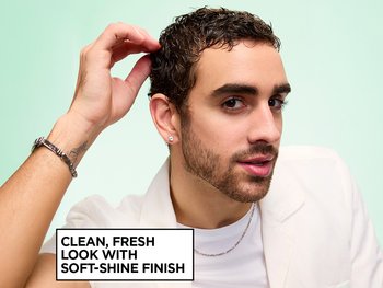 Garnier Fructis Style model running his fingers through damp, defined dark curls defined and styled with Pure Clean Styling Gel and Finishing Paste, while wearing a white blazer and silver chain necklace, next to on-image text reading "CLEAN, FRESH LOOK WITH SOFT-SHINE FINISH," set against a mint green background.