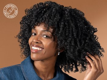 Model smiling while holding her healthy coily hair in Glossy Curl Color Vinyl Licorice.