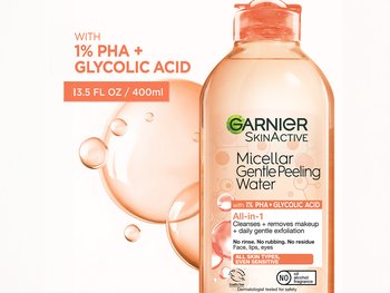 A bottle of Garnier SkinActive Micellar Gentle Peeling Water with an orange cap, highlighting "1% PHA + GLYCOLIC ACID" for daily gentle exfoliation. Orange bubbles are in the background.