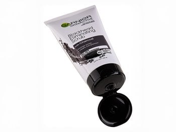 A white tube of Garnier SkinActive Blackhead Eliminating Scrub with Charcoal, lying on its side with the cap open, showing its texture.