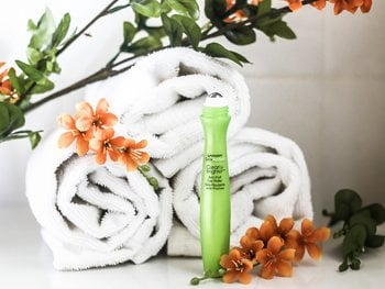 A green Garnier SkinActive Clearly Brighter Eye Roller placed on white rolled towels, surrounded by orange flowers and green leaves.