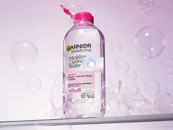 A bottle of Garnier SkinActive Micellar Cleansing Water (pink cap) surrounded by floating bubbles, against a light pink background.