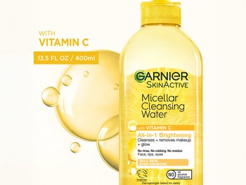 A bottle of Garnier SkinActive Micellar Cleansing Water with a yellow cap, labeled "All-in-1 Brightening with Vitamin C" for dull skin, showing yellow bubbles in the background.