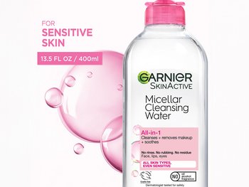 A bottle of Garnier SkinActive Micellar Cleansing Water with a pink cap, labeled "All-in-1" for sensitive skin, showing pink bubbles in the background.