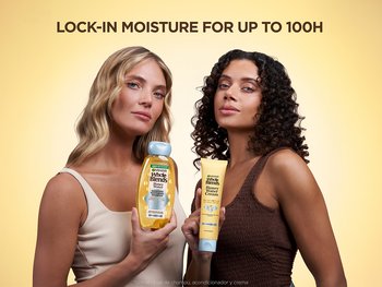 Two women stand against a warm yellow background. The woman on the left, with long blonde waves, holds a yellow and blue Garnier Whole Blends Honey Water shampoo bottle. The woman on the right, with dark curly hair, holds a tube of Garnier Whole Blends Honey Cream. Text above reads "LOCK-IN MOISTURE FOR UP TO 100H," and text below indicates use with shampoo, conditioner, and cream.