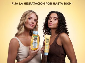 Two women stand against a warm yellow background. The woman on the left, with long blonde waves, holds a yellow and blue Garnier Whole Blends Honey Water shampoo bottle. The woman on the right, with dark curly hair, holds a tube of Garnier Whole Blends Honey Cream. Text above reads "LOCK-IN MOISTURE FOR UP TO 100H," and text below indicates use with shampoo, conditioner, and cream.