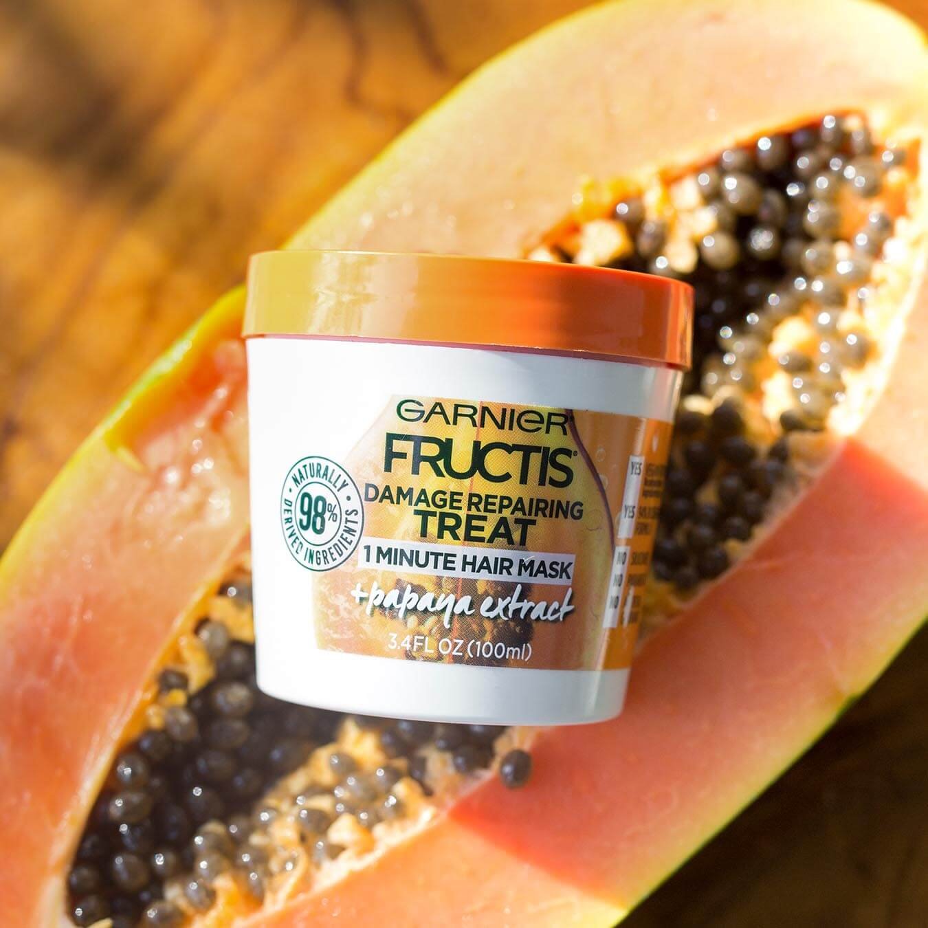 Garnier Fructis Damage Repairing Treat 1 Minute Hair Mask with Papaya Extract sitting on half a papaya on a wooden table.
