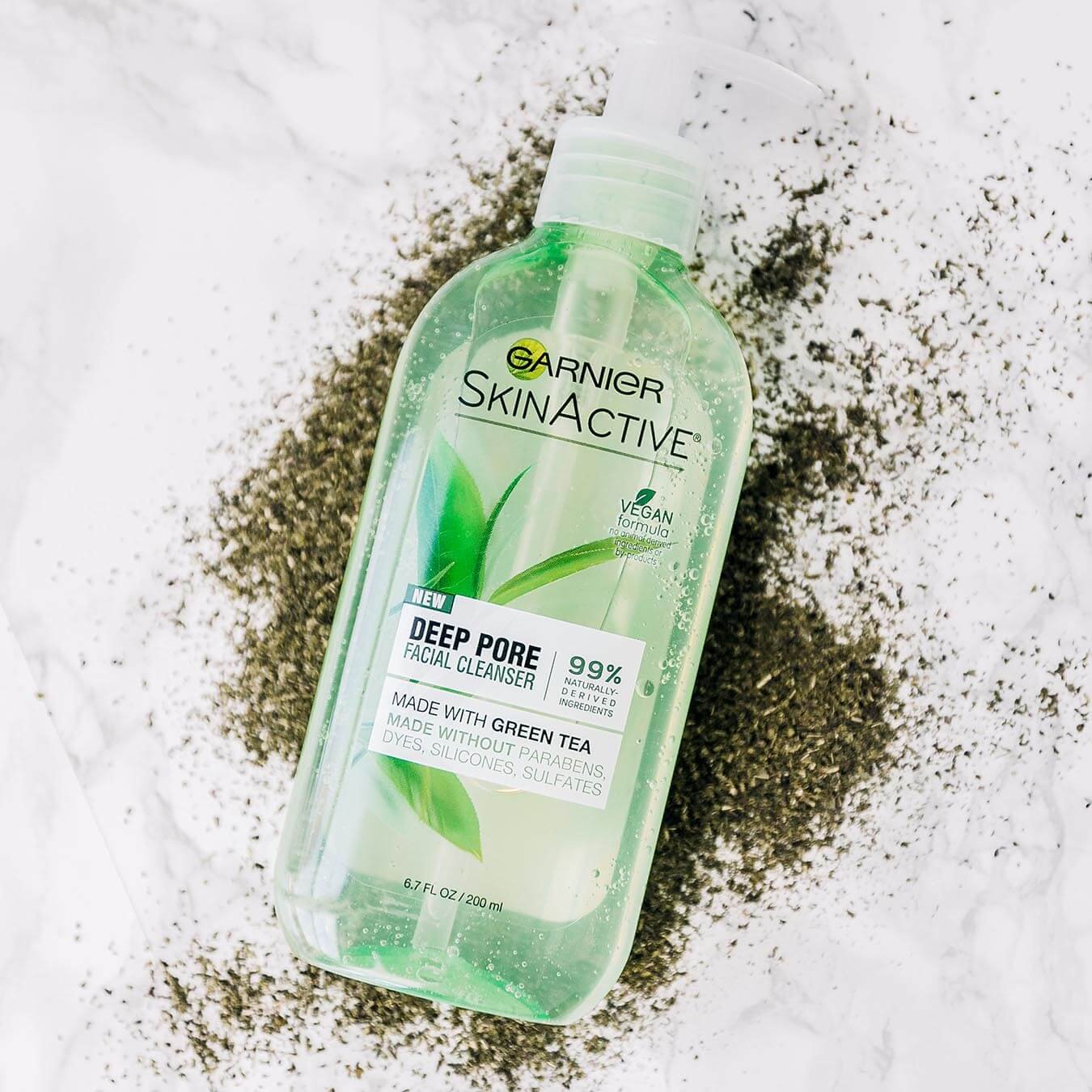 Garnier SkinActive Deep Pore Facial Cleanser with Green Tea on a pile of powdered green tea on white marble.