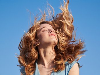 A woman with long, wavy blond hair throws her head back.