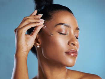 Studio shot of a young woman applying an oil to her face against a blue background