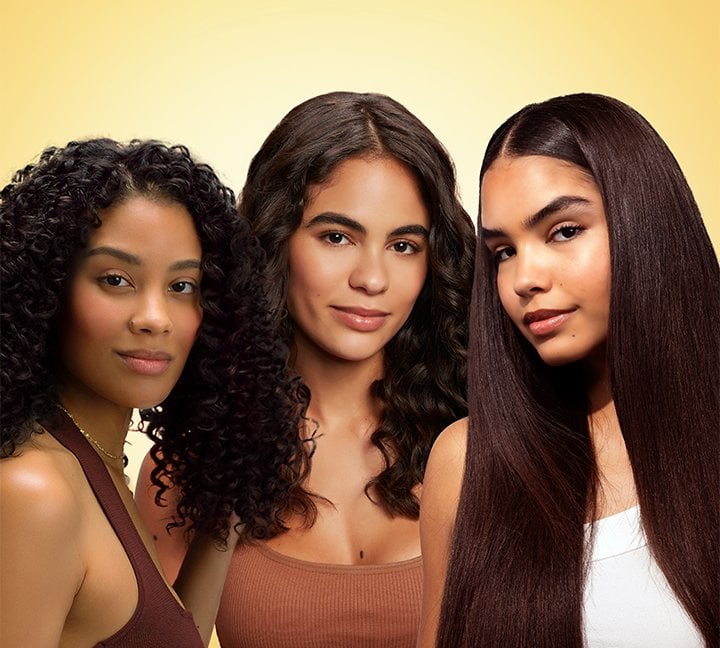Diverse group of three women with healthy, shiny dark hair showcasing curly, wavy, and straight hair textures achievable with Garnier hair care treatments for nourished and healthy results.