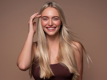 Blond woman with sleek, straight, anti-frizz hair smiles.