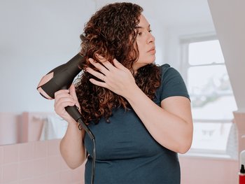 Curly haired women blow dries her hair.