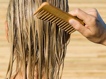 Back shot of model's head - a hand is running a wooden wide-tooth comb through her blonde wet hair.