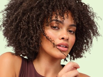 Female model with coily dark brown hair holding a strand of curly hair in her right hand
