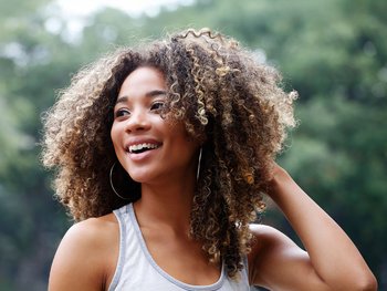 A woman with curly, brown hair smiles outside.