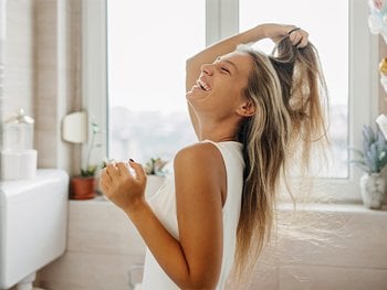 Woman with blonde hair combs her hair with her fingers as she laughs.