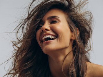 Front shot of brunette woman smiling. She has brown, flowy, smooth, shiny hair.