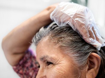 Female with long brown hair applying hair color product to her roots