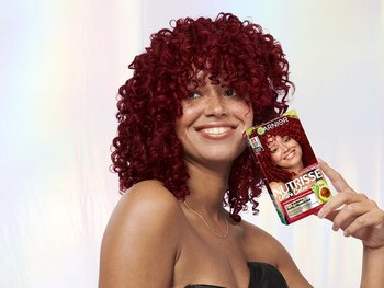 Model with red hair posing next to Garnier hair color box