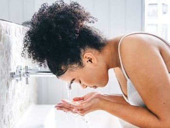 Dark-skinned model washing face at a sink