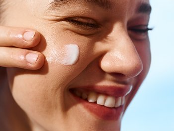 Light skinned model applying moisturizer to cheek