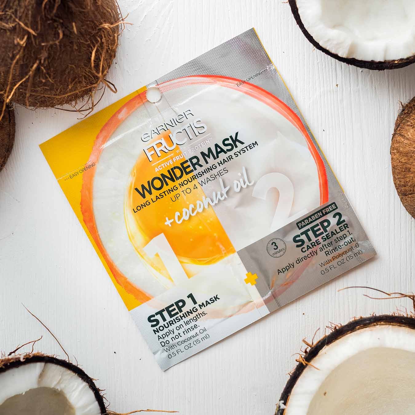Garnier Fructis Wonder Mask with Coconut Oil on white-painted wood and halved coconuts.