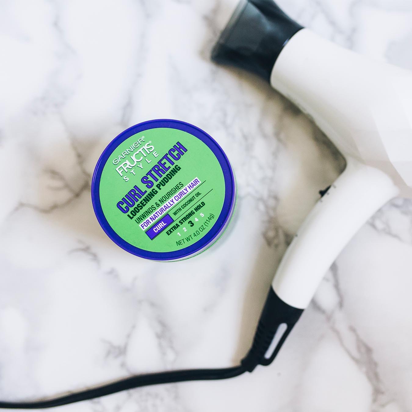 Garnier Fructis Style Curl Stretch Loosening Pudding on white marble next to a white and black blow dryer.