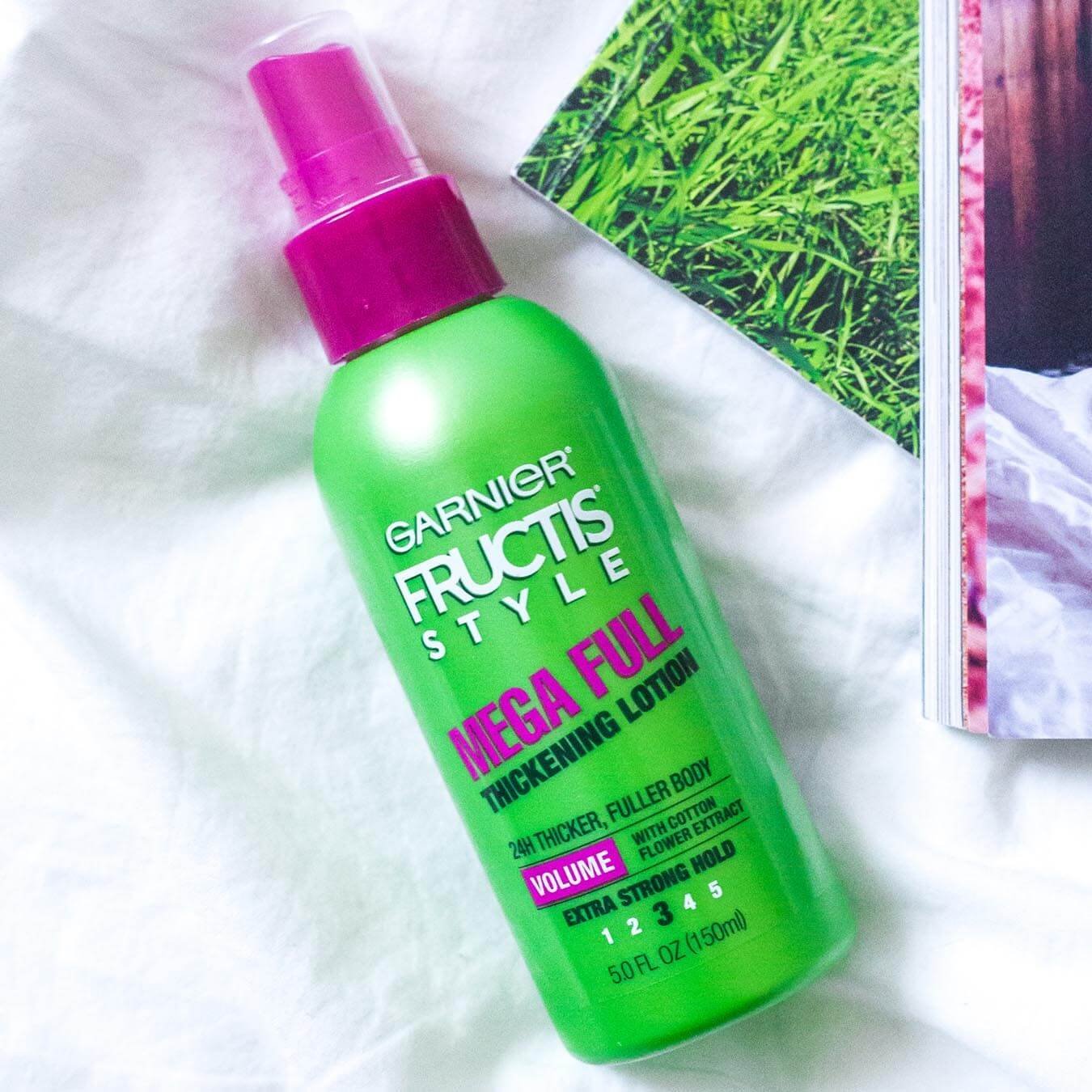 Garnier Fructis Style Mega Full Thickening Lotion on white cotton next to a picture of grass and an open magazine.