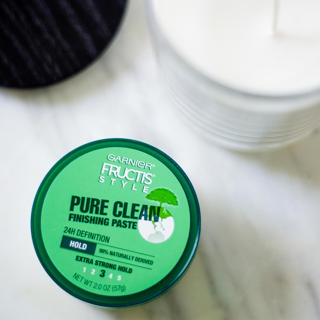 Garnier Fructis Style Pure Clean Finishing Paste on white marble next to a white candle and black lid.
